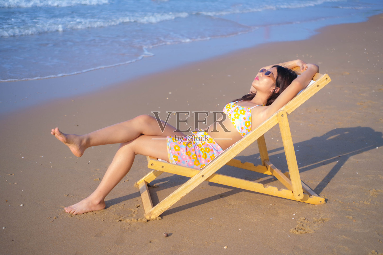 年轻的亚洲女子穿着泳衣坐在沙滩上晒日光浴。照片摄影图片