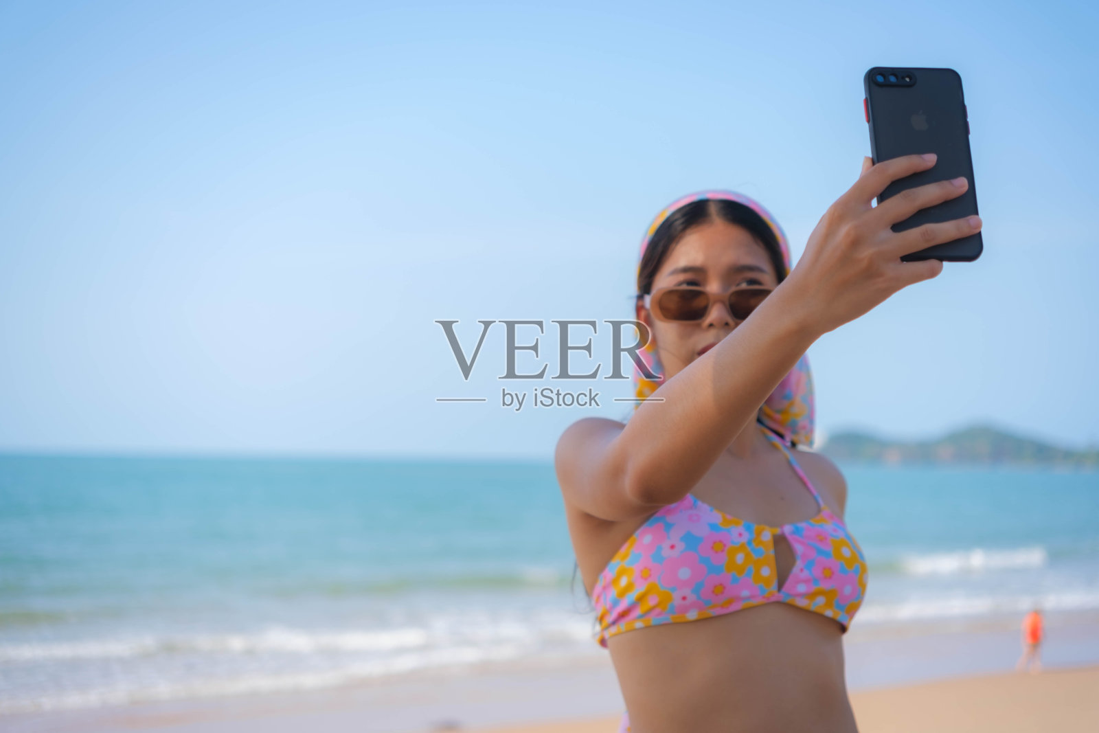 穿着泳装的年轻亚洲女子在沙滩上玩手机照片摄影图片