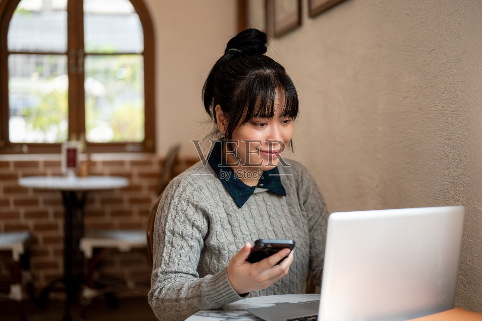 一位面带微笑、积极向上的年轻亚洲女性正在一家咖啡店用笔记本电脑远程办公。照片摄影图片