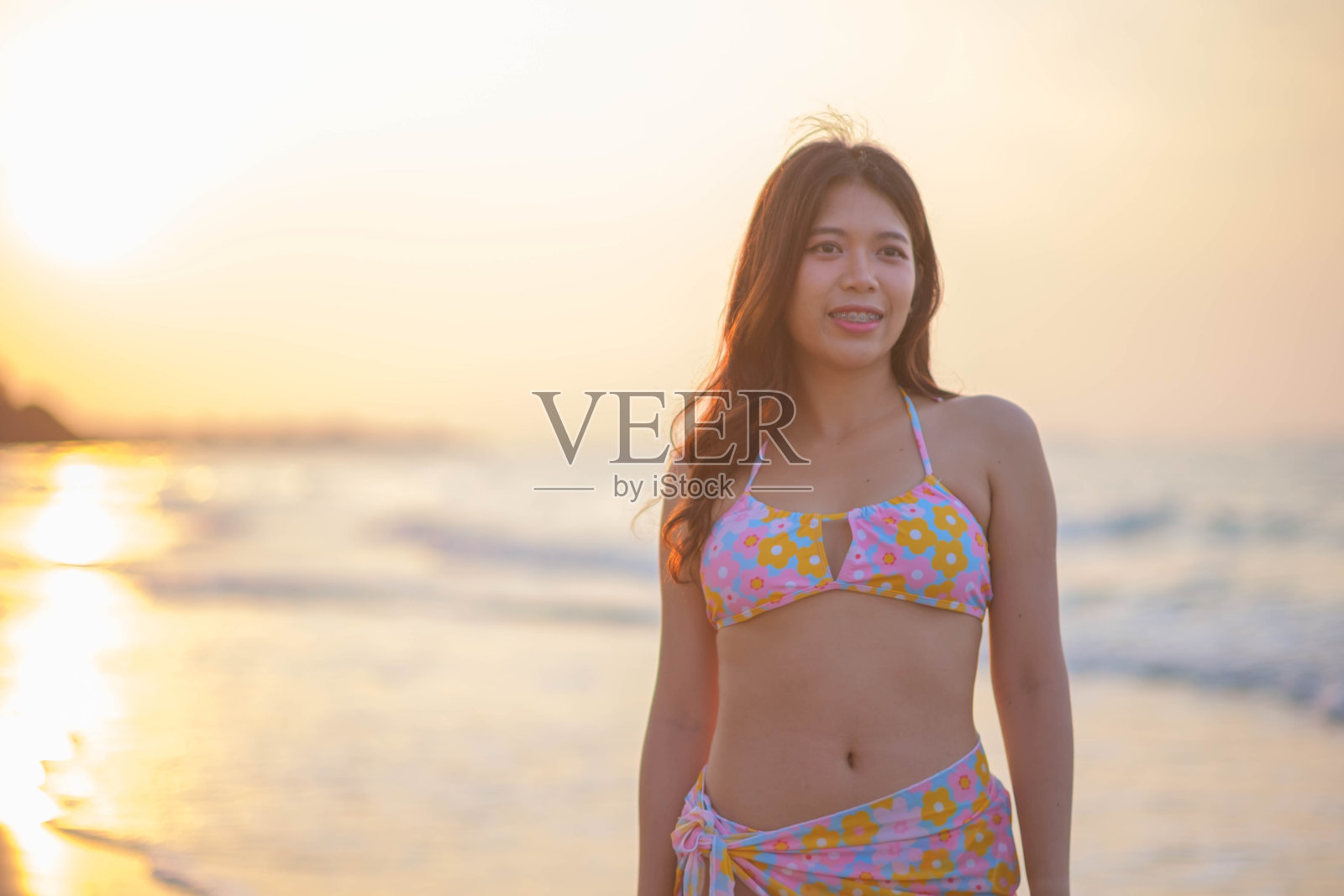 穿着泳装走在沙滩上的年轻亚洲女子在早晨看日出照片摄影图片