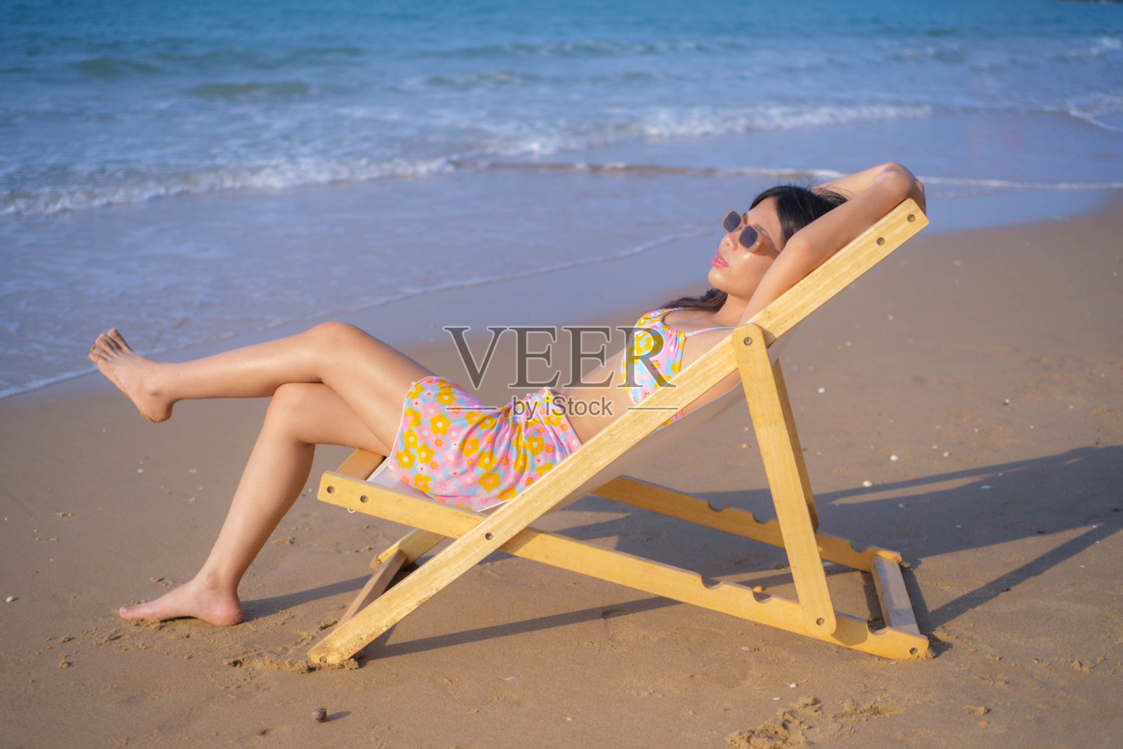 年轻的亚洲女子穿着泳衣坐在沙滩上晒日光浴。照片摄影图片