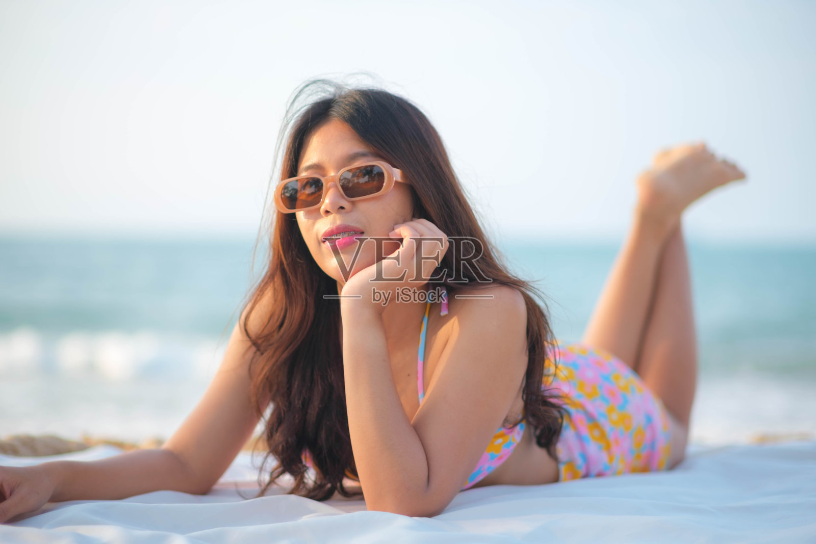 穿着泳装的年轻亚洲女子躺在沙滩上的床单上照片摄影图片