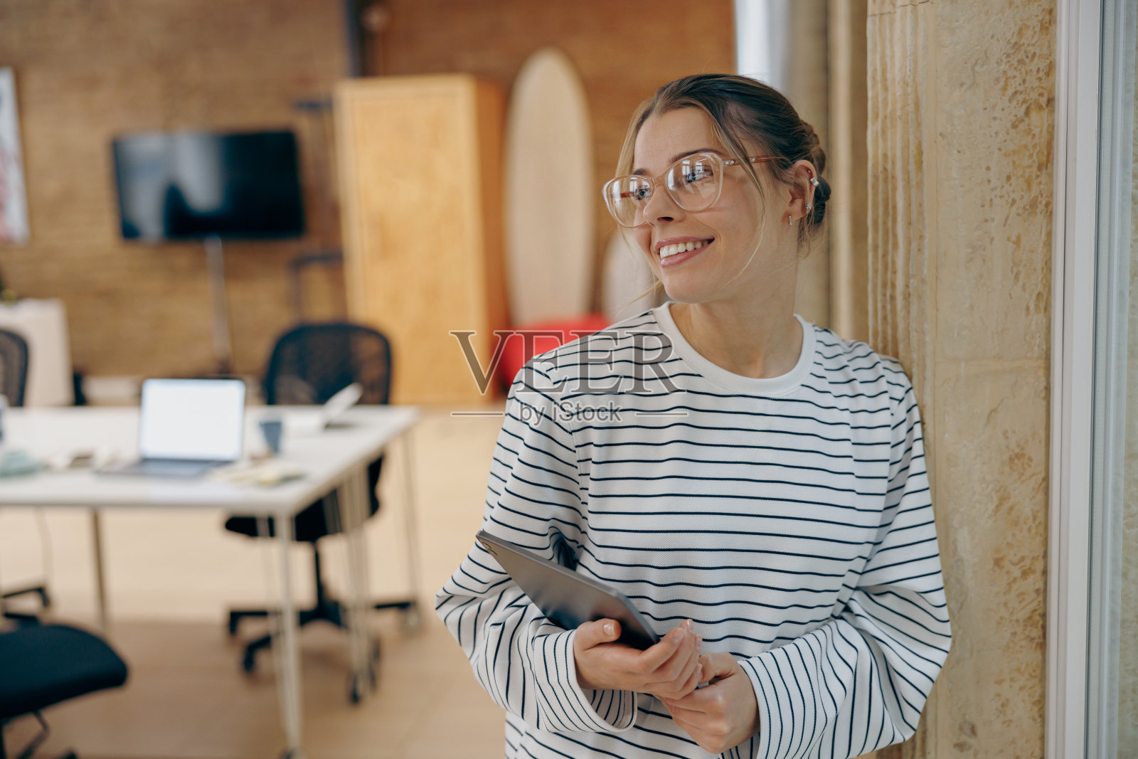 微笑的女性营销人员拿着数码平板电脑，站在时尚的联合办公场所，望向别处照片摄影图片