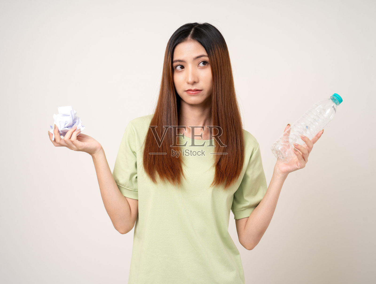 年轻的亚洲美女拿着纸和塑料瓶进行分类，然后把它们扔进垃圾桶。积极的环保女性，穿着绿色衬衫，有着回收和可持续发展的理念。照片摄影图片