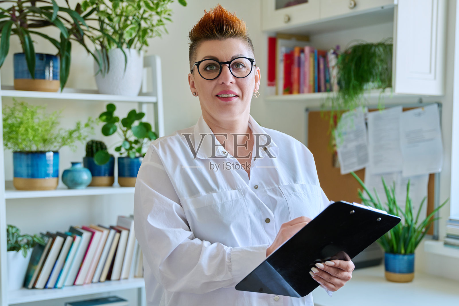 微笑的中年女性心理治疗师的肖像，办公室里有剪贴板照片摄影图片