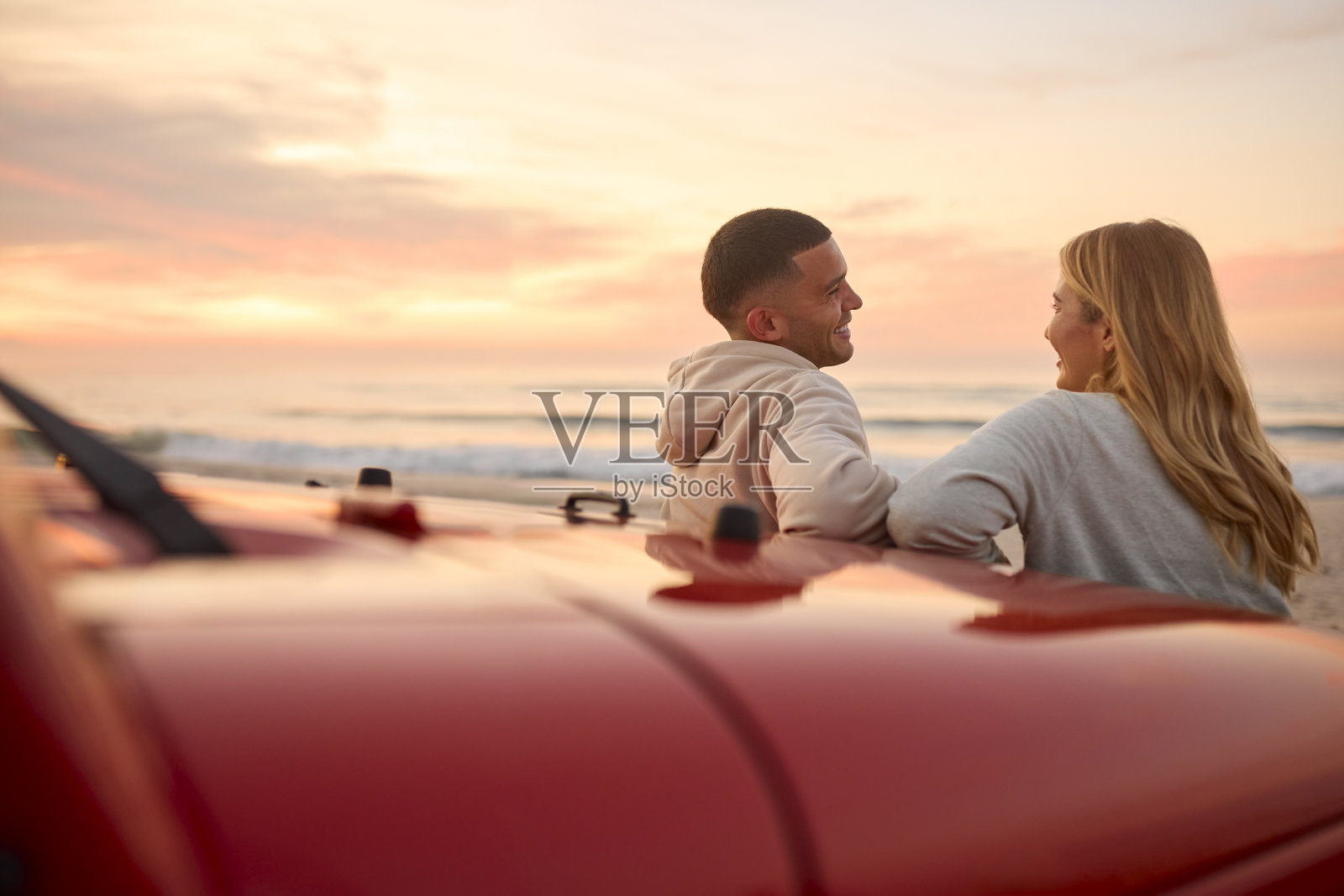 年轻夫妇在沙滩上聊天，一起看日出的后景照片摄影图片