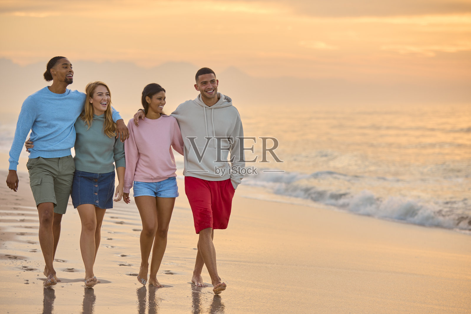 一对情侣和朋友穿着休闲服，在黎明时分沿着海滩海岸线散步照片摄影图片