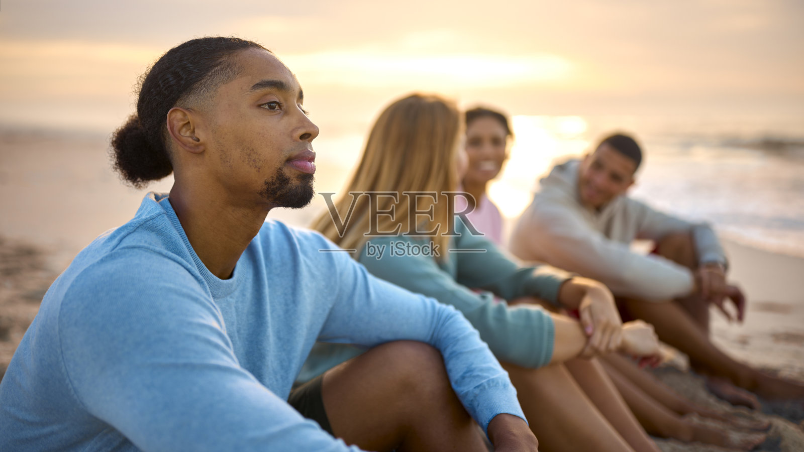 年轻夫妇和朋友穿着休闲装度假，坐在沙滩上一起看日出照片摄影图片