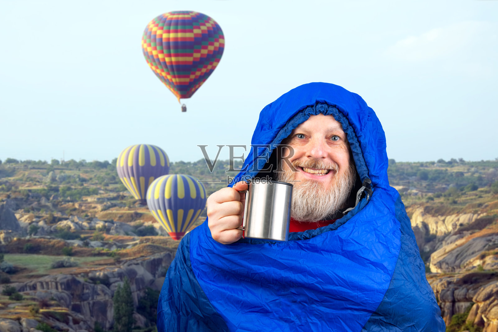 快乐的大胡子男人躺在睡袋里，拿着一杯咖啡，在山间的自然背景下。大自然在山间漫步照片摄影图片