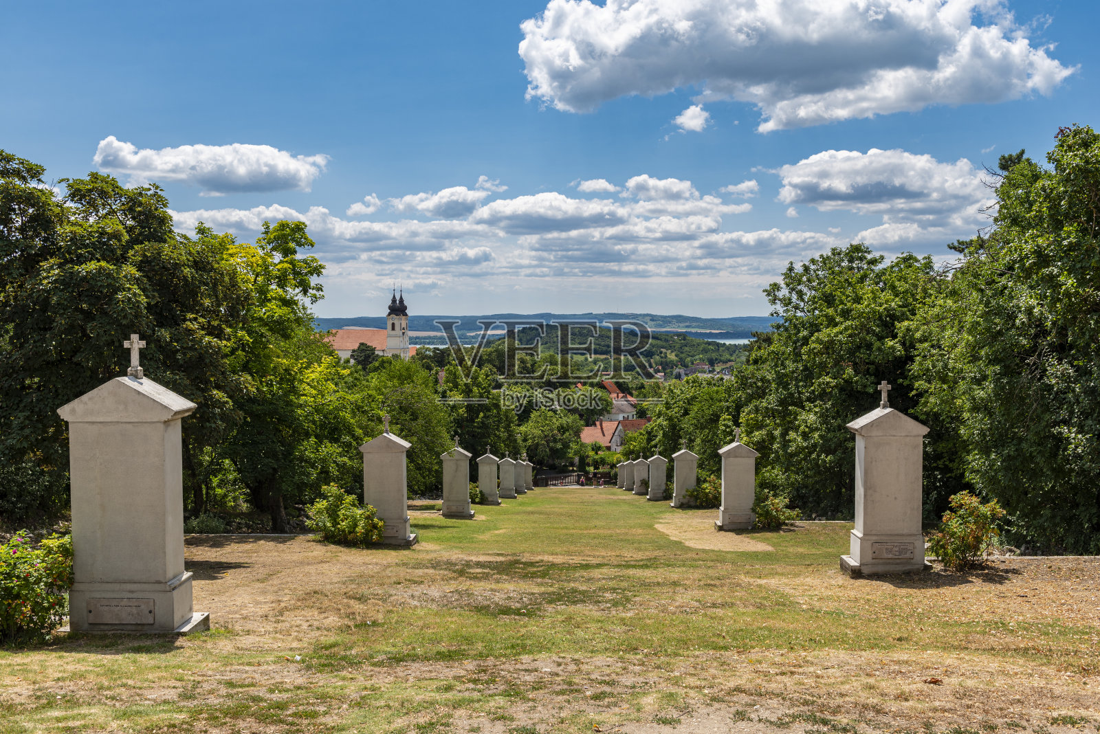 从髑髅地沿着一排纪念石头向下看匈牙利的蒂哈尼，巴拉顿湖和它的本笃会修道院在晴朗的夏日天气和晴朗的云照片摄影图片