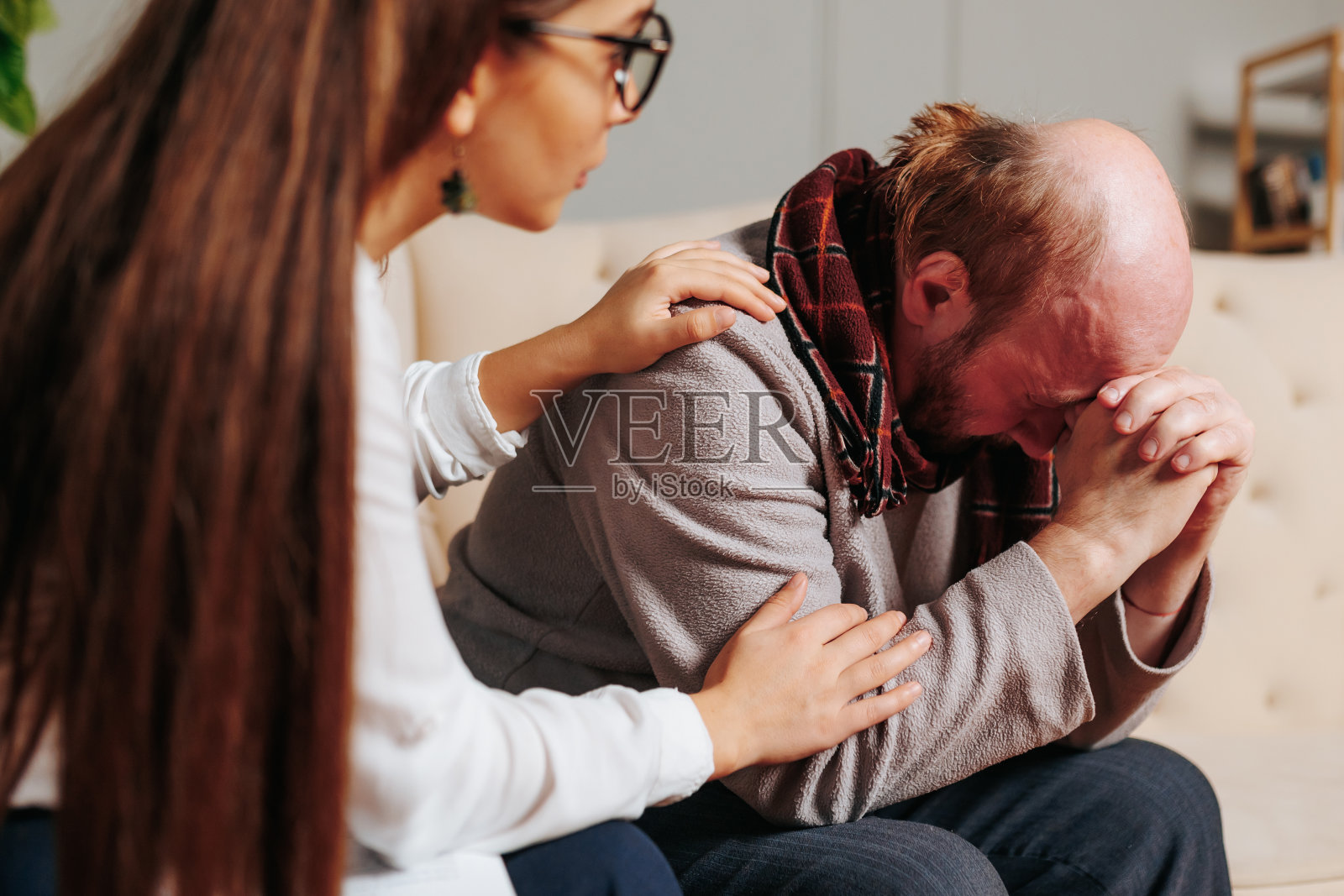 年轻的女心理学家把她的手放在办公室里抑郁的老人的肩膀上。照片摄影图片