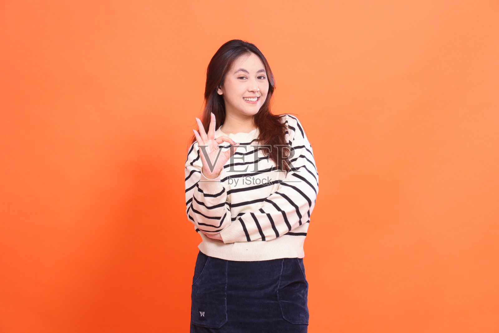 美丽的亚洲女人自信开朗地微笑着，双臂交叉站在那里做手势，很酷，穿着白色毛衣，在橙色的背景下看着镜头照片摄影图片