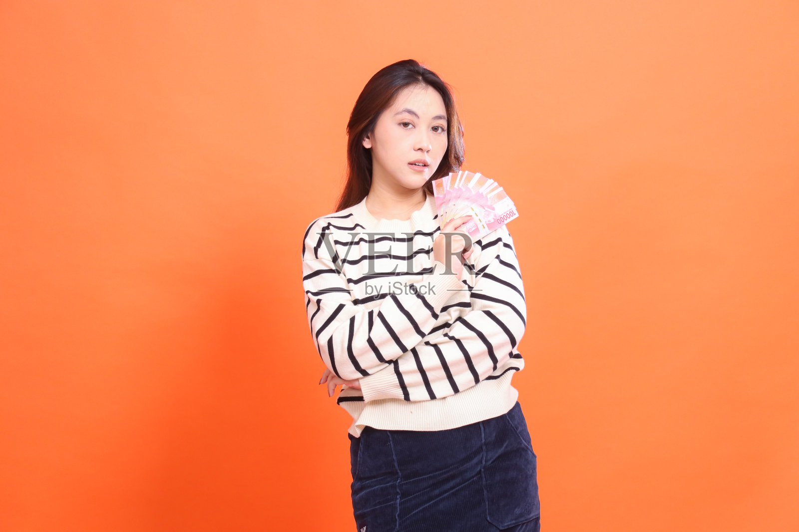 一位优雅的印度尼西亚妇女站在那里，手里拿着一些印尼盾进行交易。以时尚、商业、金融为理念照片摄影图片