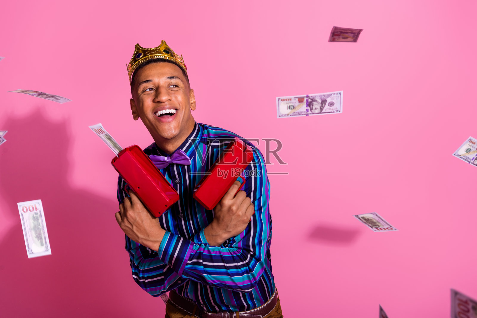 照片时髦开朗的家伙穿条纹衬衫金色皇冠射击钱枪孤立的粉红色背景照片摄影图片