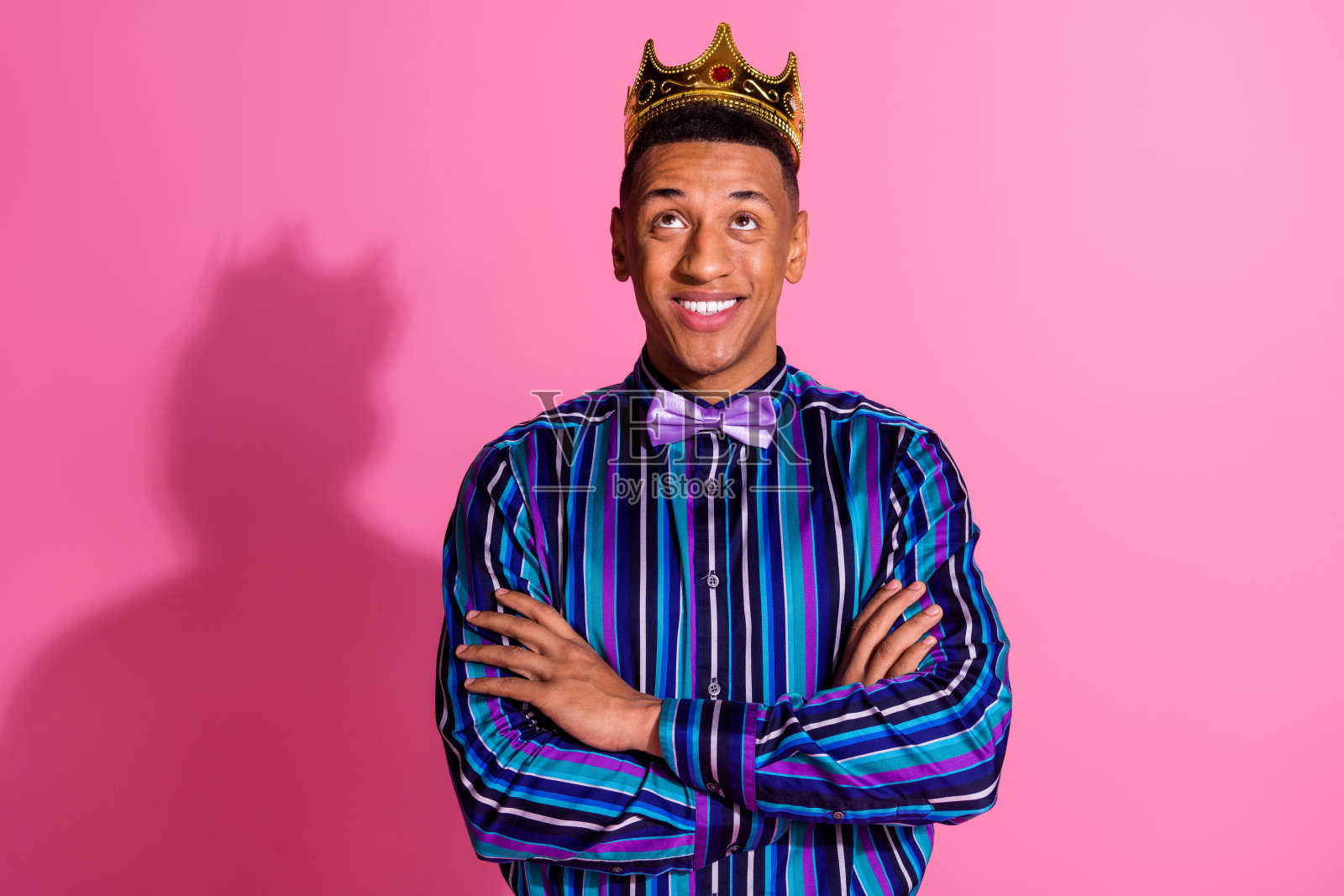 照片积极梦幻的家伙穿条纹衬衫金色皇冠双臂折叠仰望空空间孤立的粉红色背景照片摄影图片
