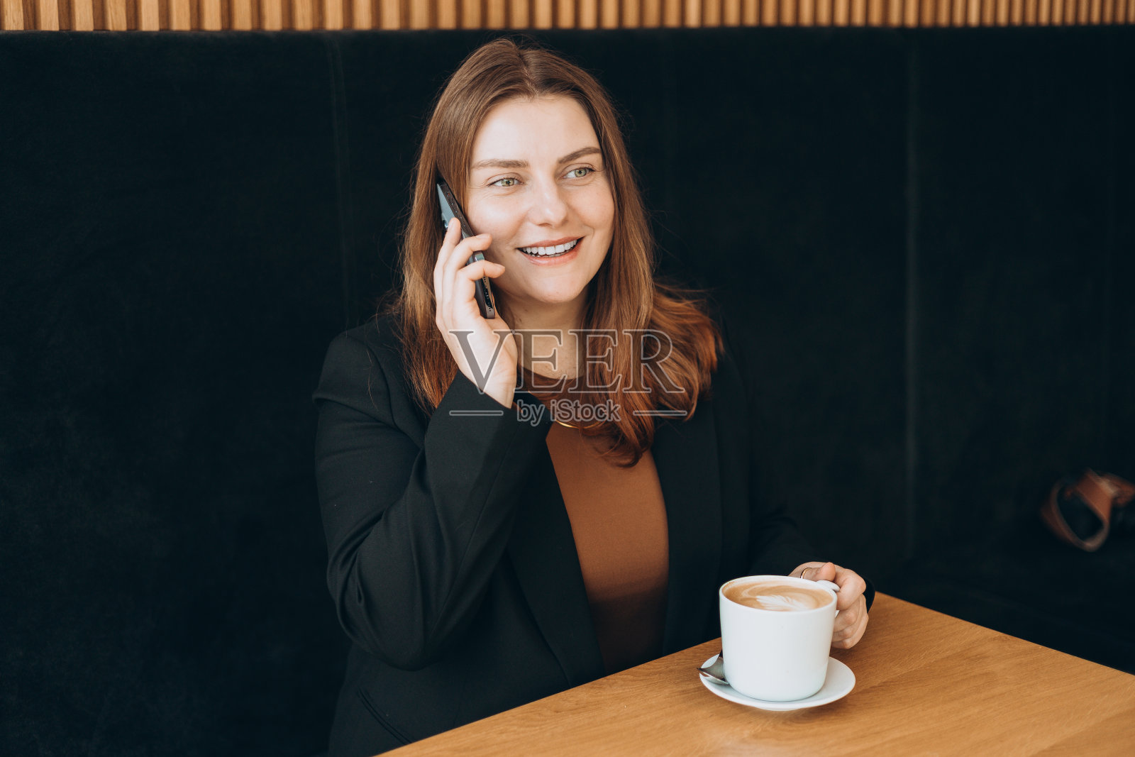 开朗的年轻红发女人穿着时尚的办公室服装在讲手机，30多岁的女孩在咖啡馆工作。女工在室内使用手机。照片摄影图片