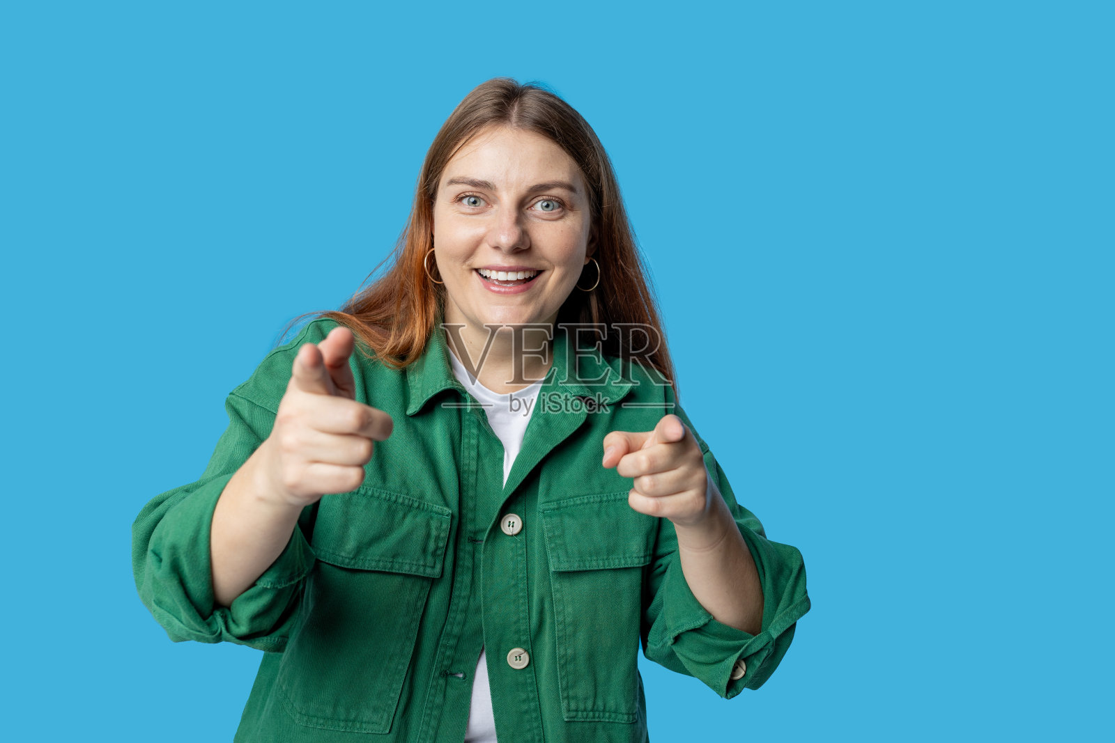 年轻微笑的快乐有趣的女人指着相机对你说，做它激励孤立的蓝色背景，工作室肖像。看着镜头，微笑着照片摄影图片