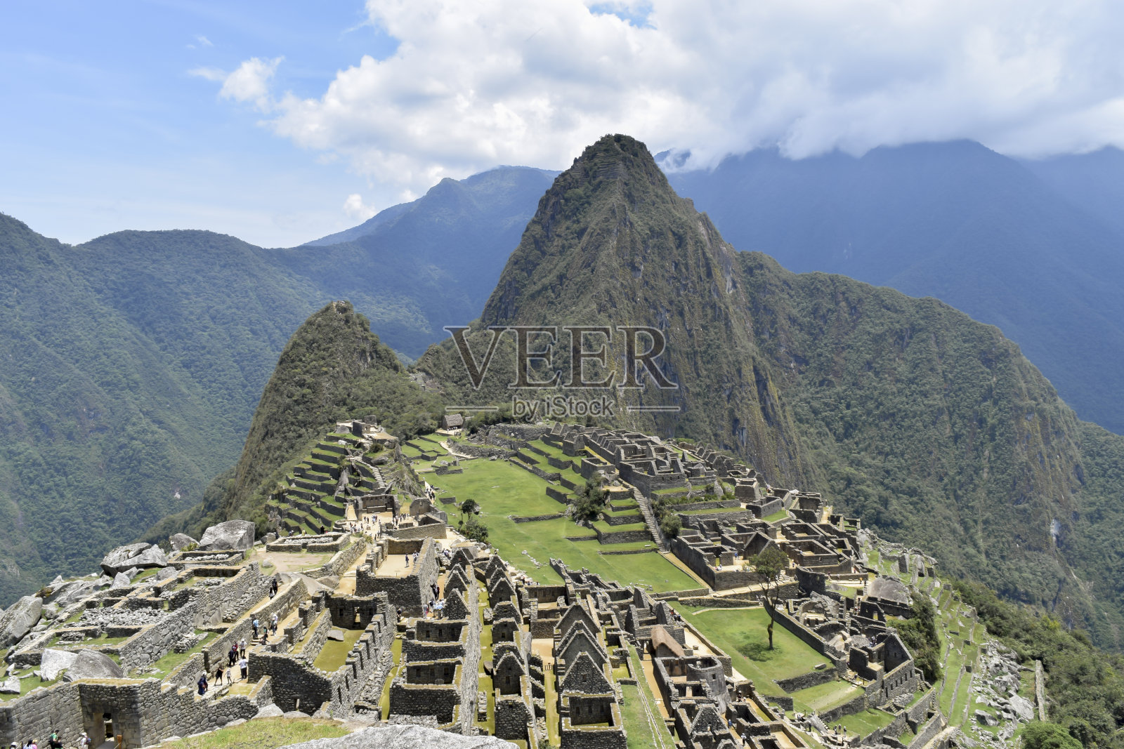 马丘比丘的废墟上有游客，有引人注目的云，世界七大奇迹之一。秘鲁库斯科，历史悠久的圣所，农业梯田的全景图，韦纳比丘和周围山脉照片摄影图片