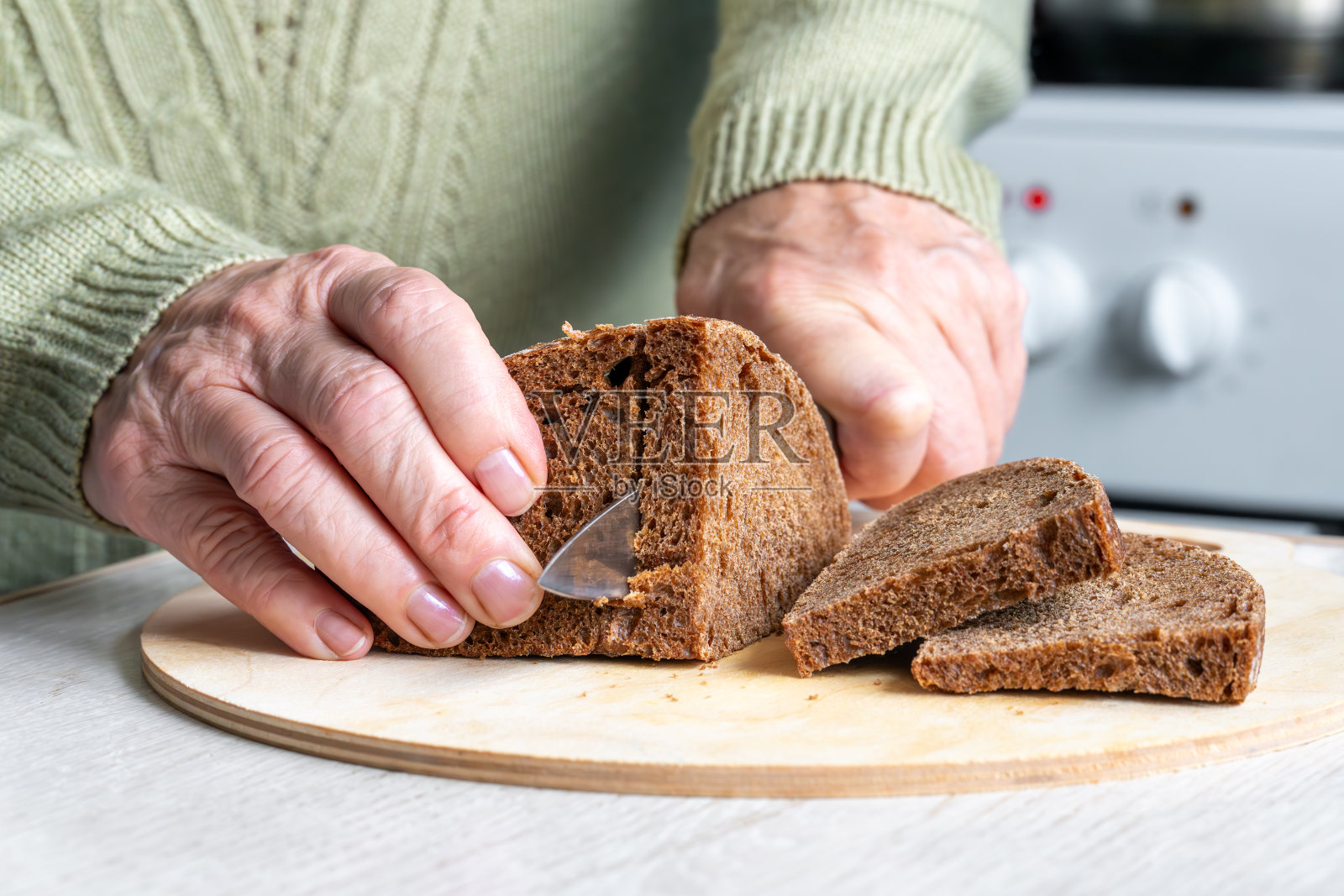 一位老人正在厨房的砧板上切黑麦面包。照片摄影图片