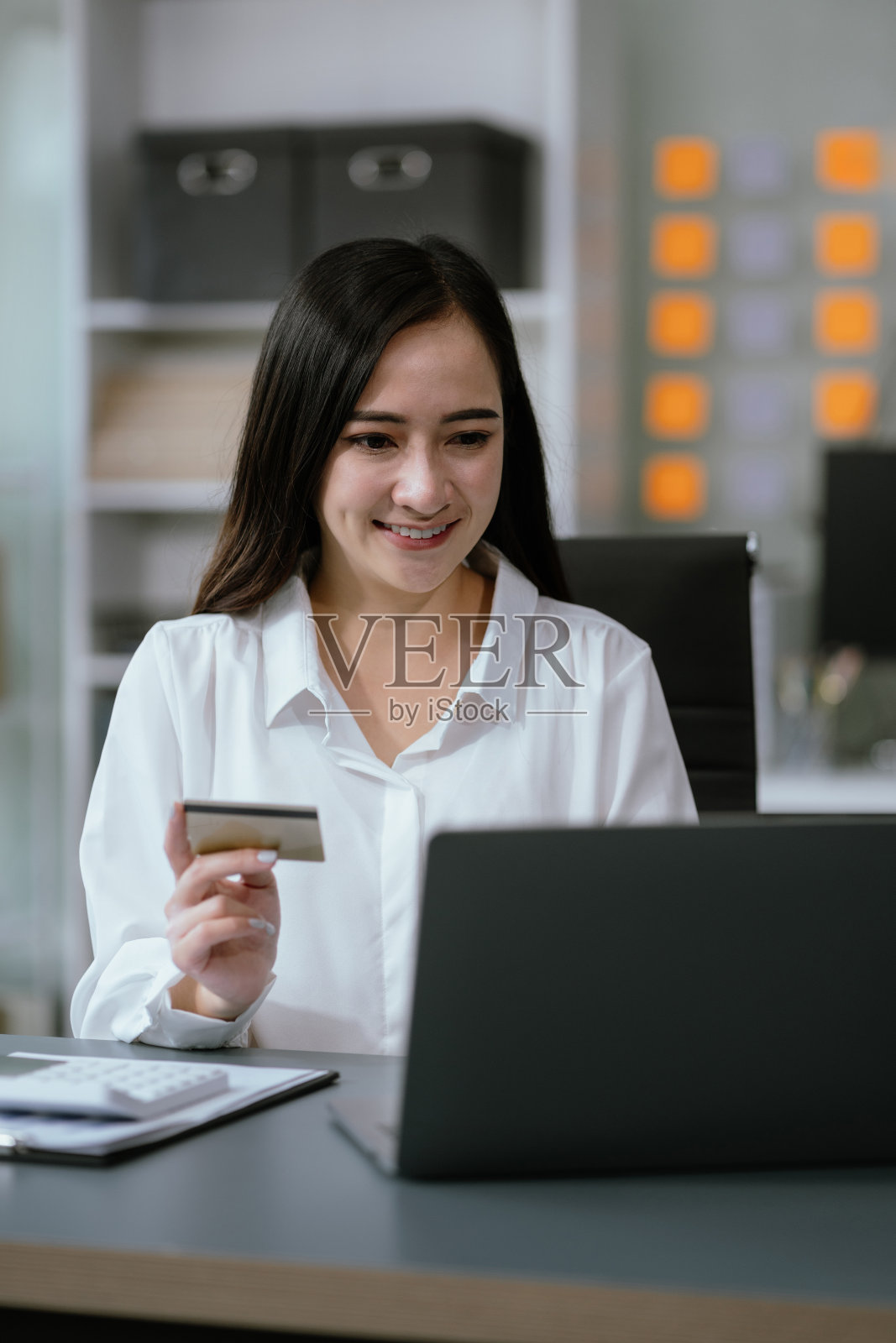 亚洲女性在家庭办公室通过电话、笔记本电脑使用信用卡进行金融交易。照片摄影图片
