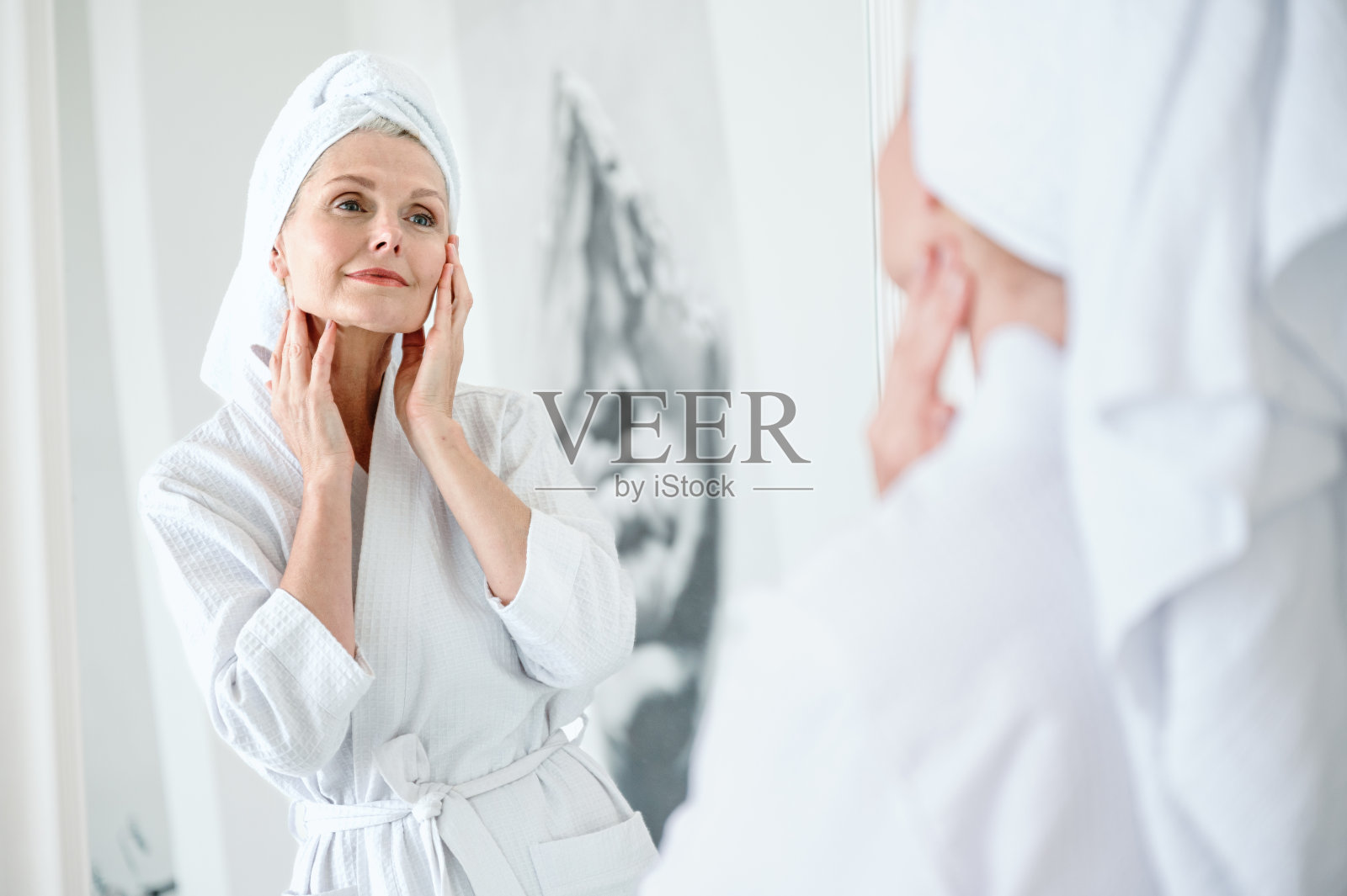 穿着长袍，皮肤完美的成熟女人看着镜子照片摄影图片