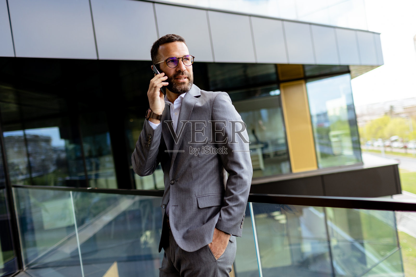 自信的商人微笑着穿着时髦的西装，映衬着现代化的玻璃幕墙。生成的人工智能照片摄影图片