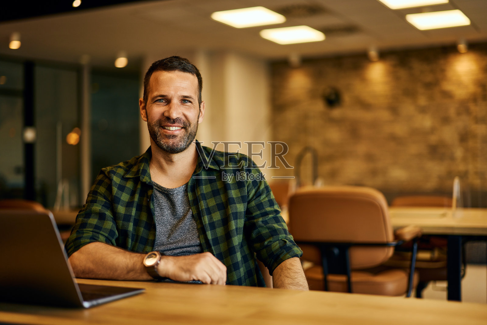 一个面带微笑的商人，坐在办公室上网工作时对着镜头摆姿势。照片摄影图片