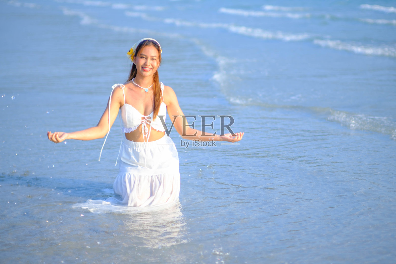 美丽的亚洲女人穿着白色的裙子坐在海边，在你的假期看起来很开心。照片摄影图片