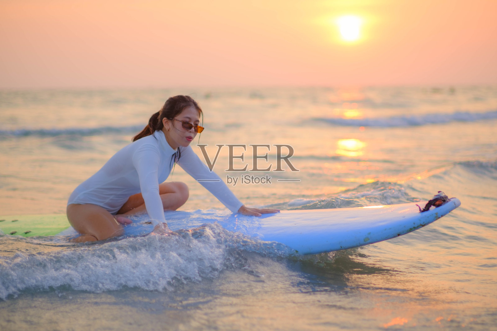 傍晚太阳落山时，年轻的亚洲女子坐在海边的冲浪板上。照片摄影图片