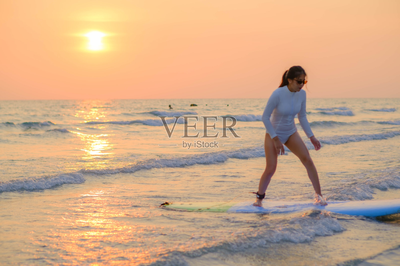 傍晚太阳落山时，年轻的亚洲女子站在海边冲浪。照片摄影图片