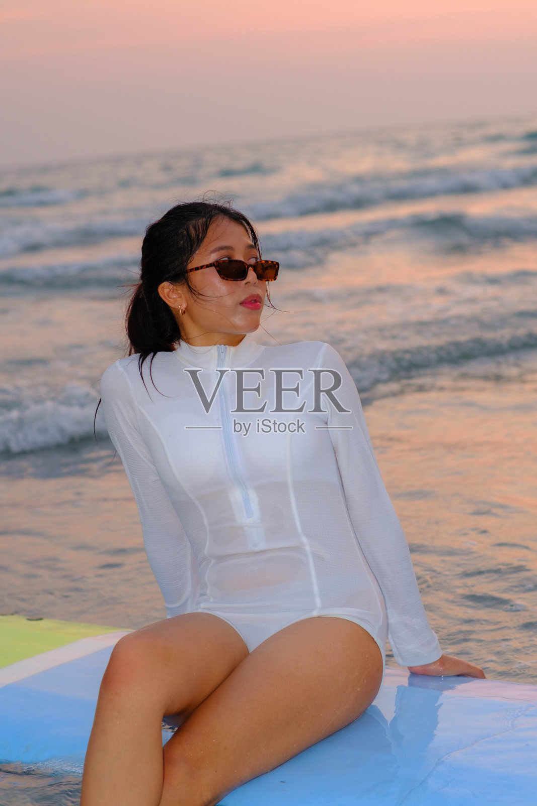 傍晚，年轻的亚洲女子坐在海边的冲浪板上照片摄影图片