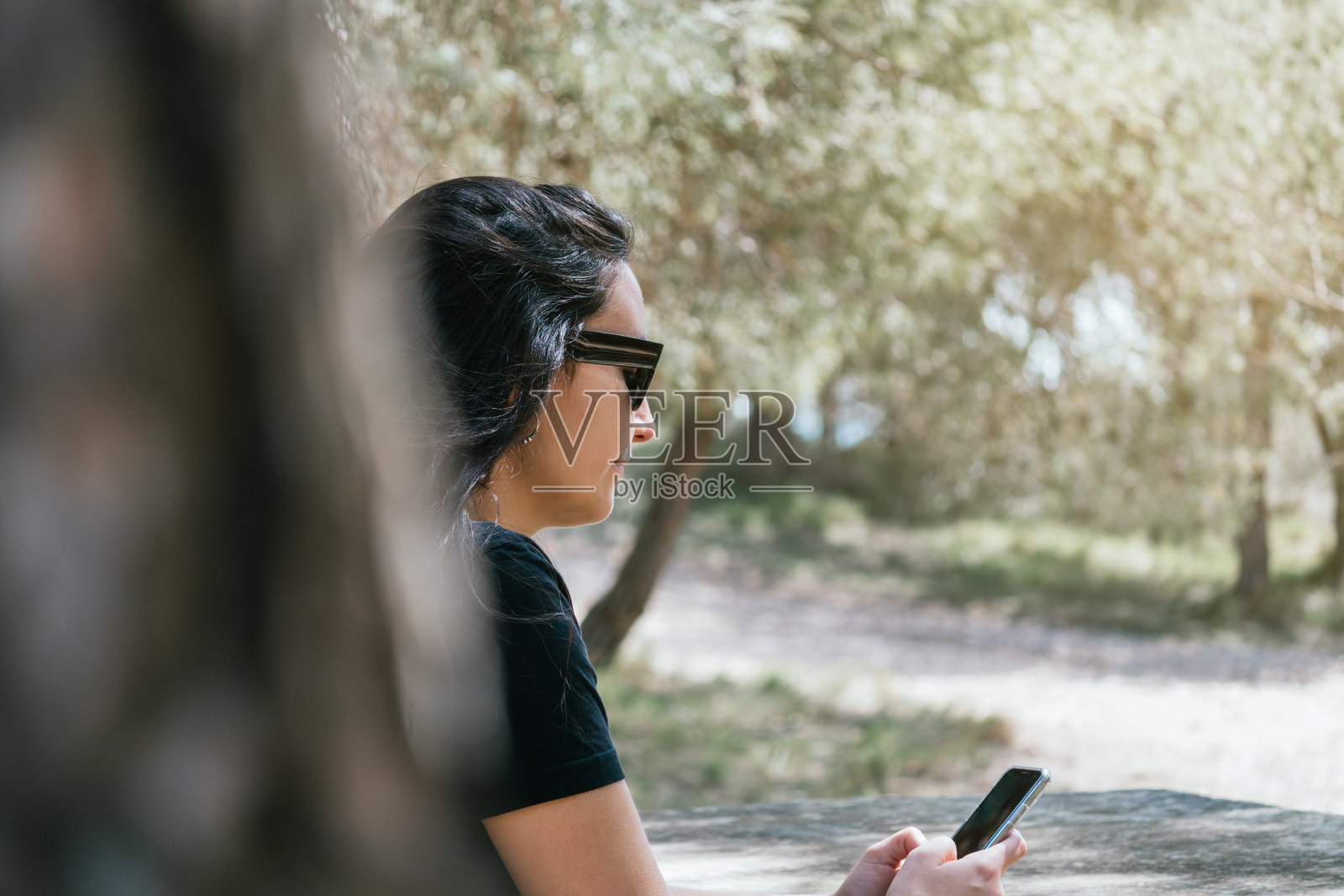 一个女人坐在一条自然小径的长凳上，看着她的手机照片摄影图片