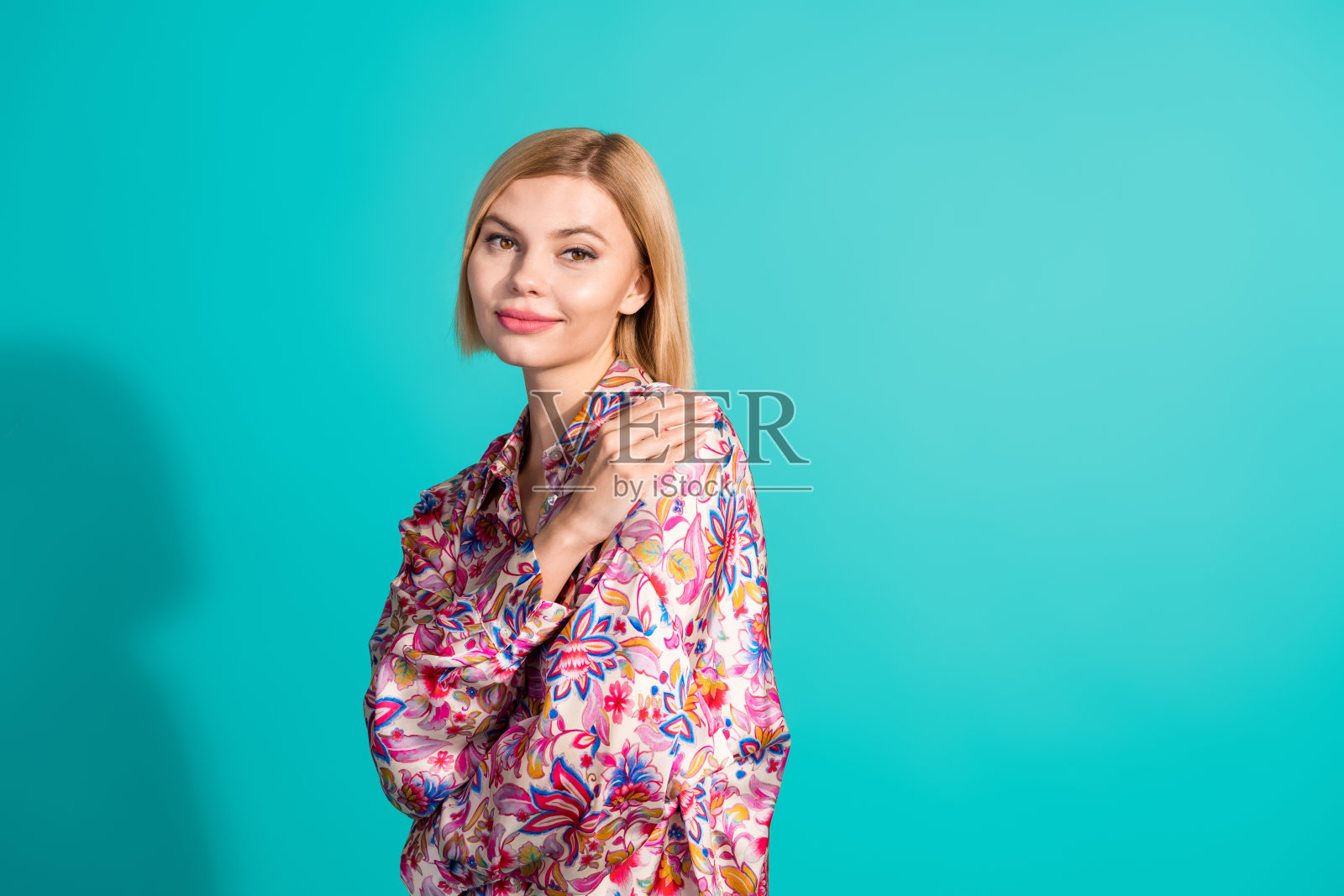 照片的华丽漂亮的女人与鲍勃发型穿着印花衬衫拥抱自己享受新鲜的衣服孤立在蓝绿色的背景照片摄影图片