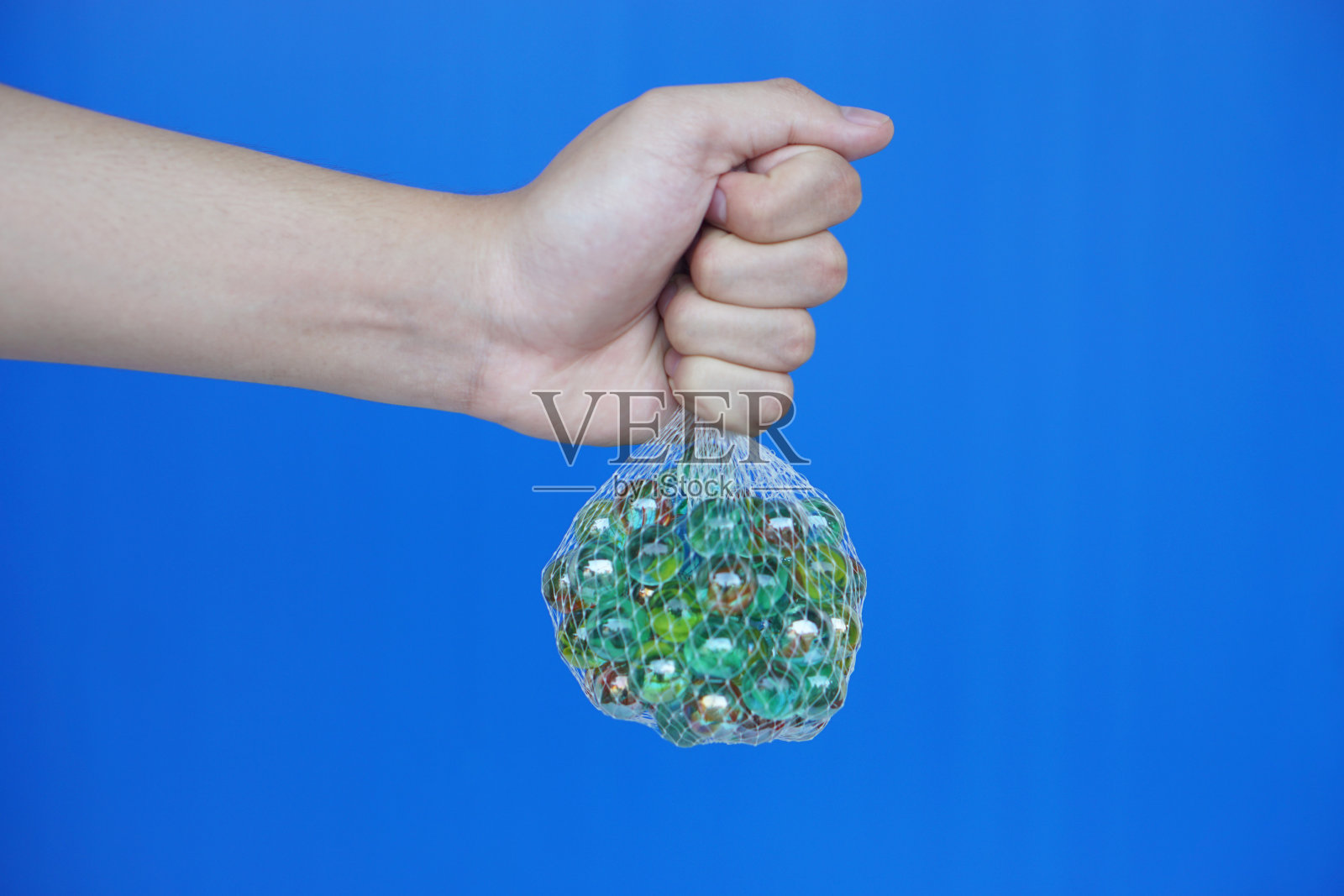 近距离手持弹珠球网袋，小的球形物体通常由玻璃制成。蓝色背景。的概念。物件可用作玩游戏的玩具或DIY工艺装饰。照片摄影图片