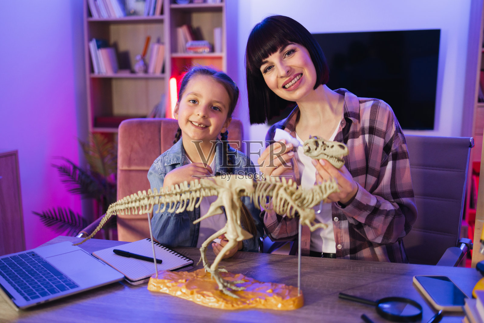 白种人母亲带着聪明可爱的女儿组装恐龙骨架。照片摄影图片