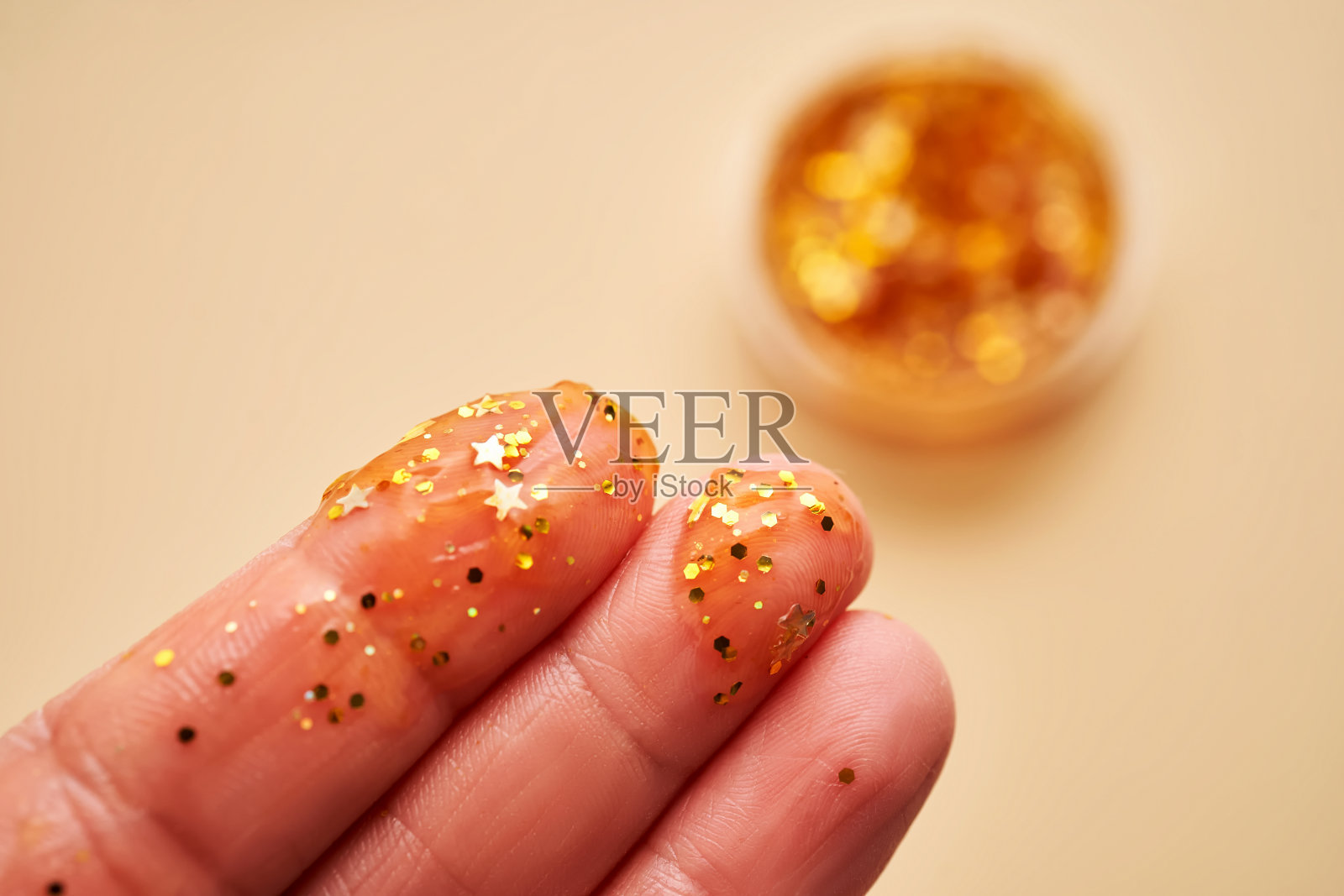 米色背景上女性手指上的亮片化妆品凝胶。照片摄影图片