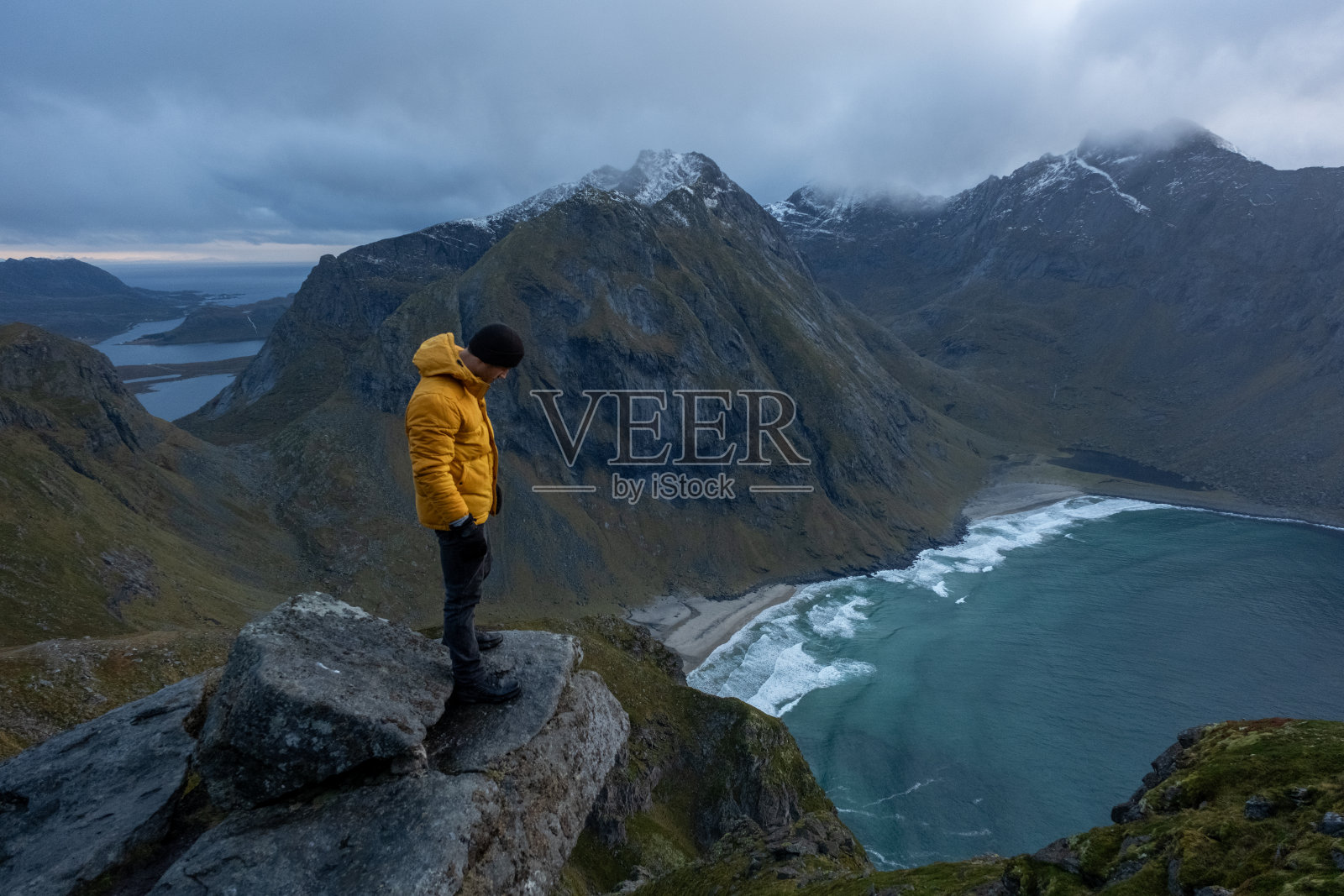 日落时分，在挪威罗弗敦的Kvalvika海滩，一名身穿黄色夹克的男子照片摄影图片