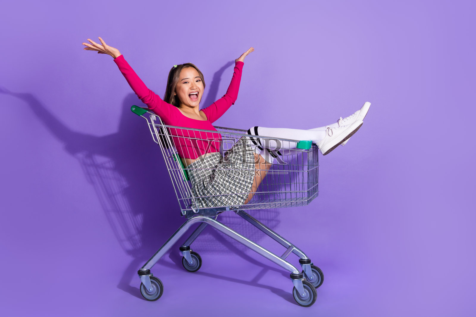 开朗印象深刻的女孩穿粉红色上衣骑购物车空的空间孤立的紫色背景的全长照片照片摄影图片