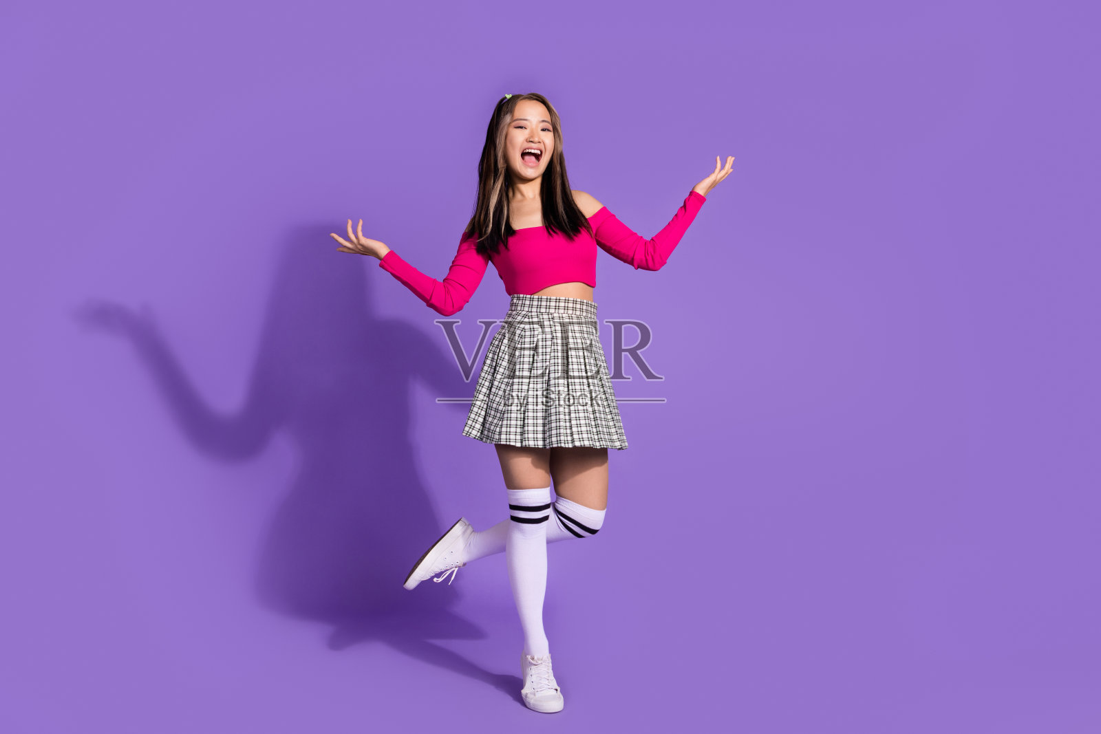 欢快的女性全身照片，穿着露脐上衣格纹裙，长袜，手掌呈现物体，在紫色背景上孤立的空白空间照片摄影图片