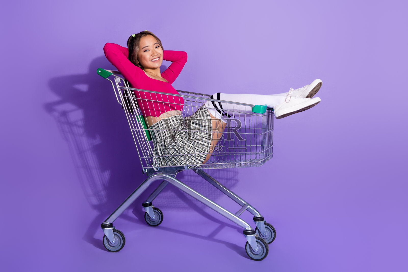 梦幻可爱的女孩全身照片穿着粉红色的上衣休息骑购物车空的空间孤立的紫色背景照片摄影图片