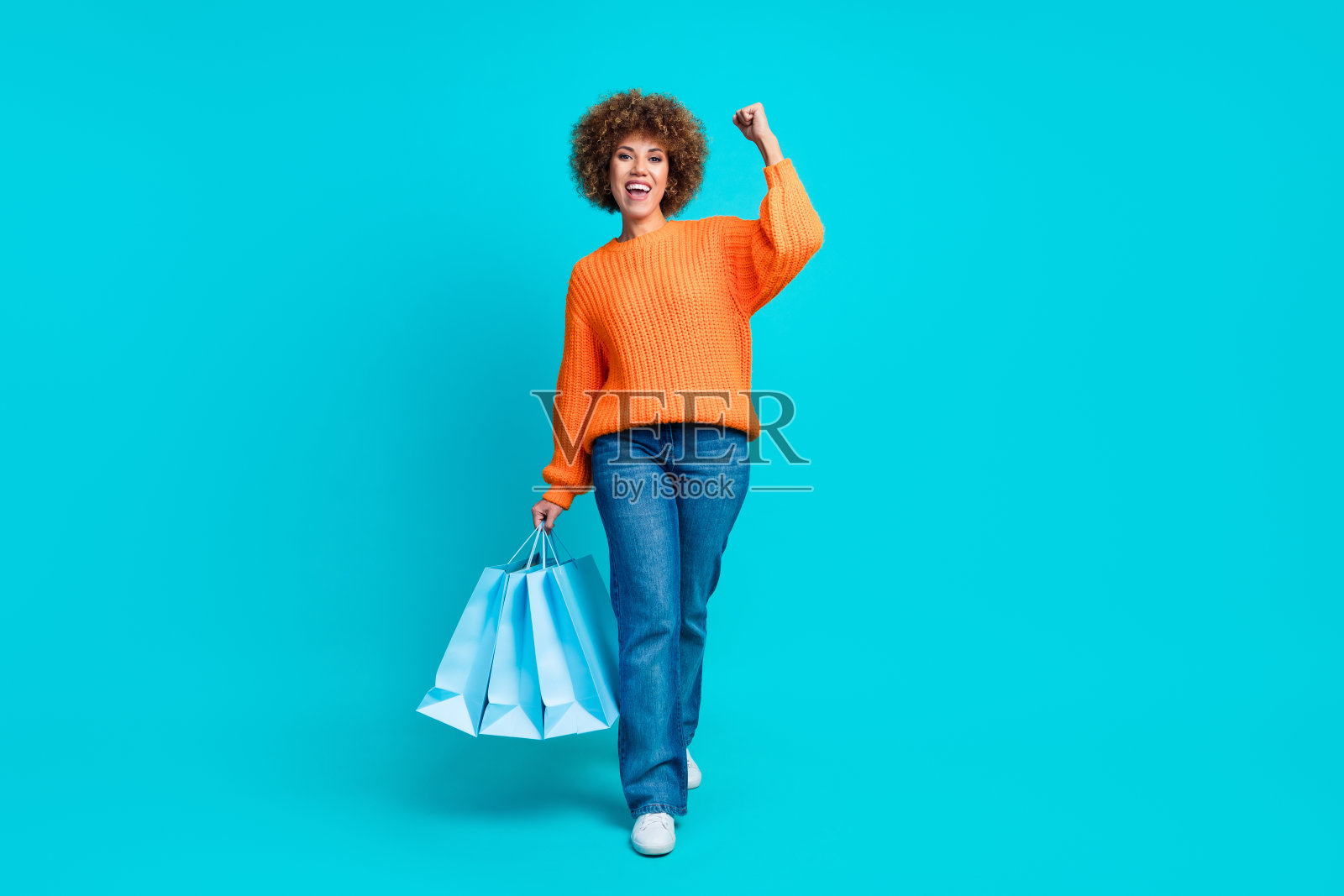 在绿松石色的背景上，漂亮欣喜的人手持购物袋举起拳头走空照片摄影图片