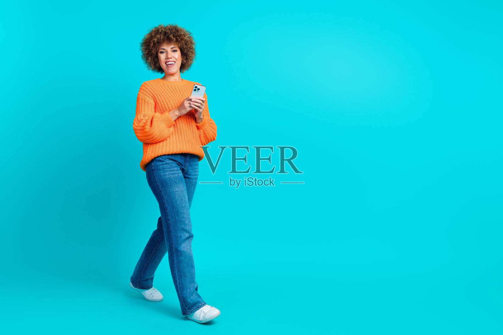 开朗可爱的拉丁女孩穿着时髦的橙色衣服走在商场中心的蓝色背景上照片摄影图片