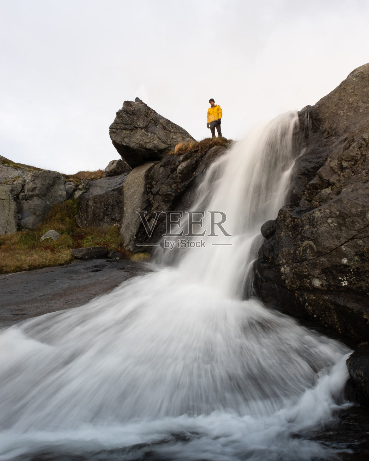 一名男子站在挪威罗弗敦的Veinestinden徒步小径上的瀑布旁照片摄影图片