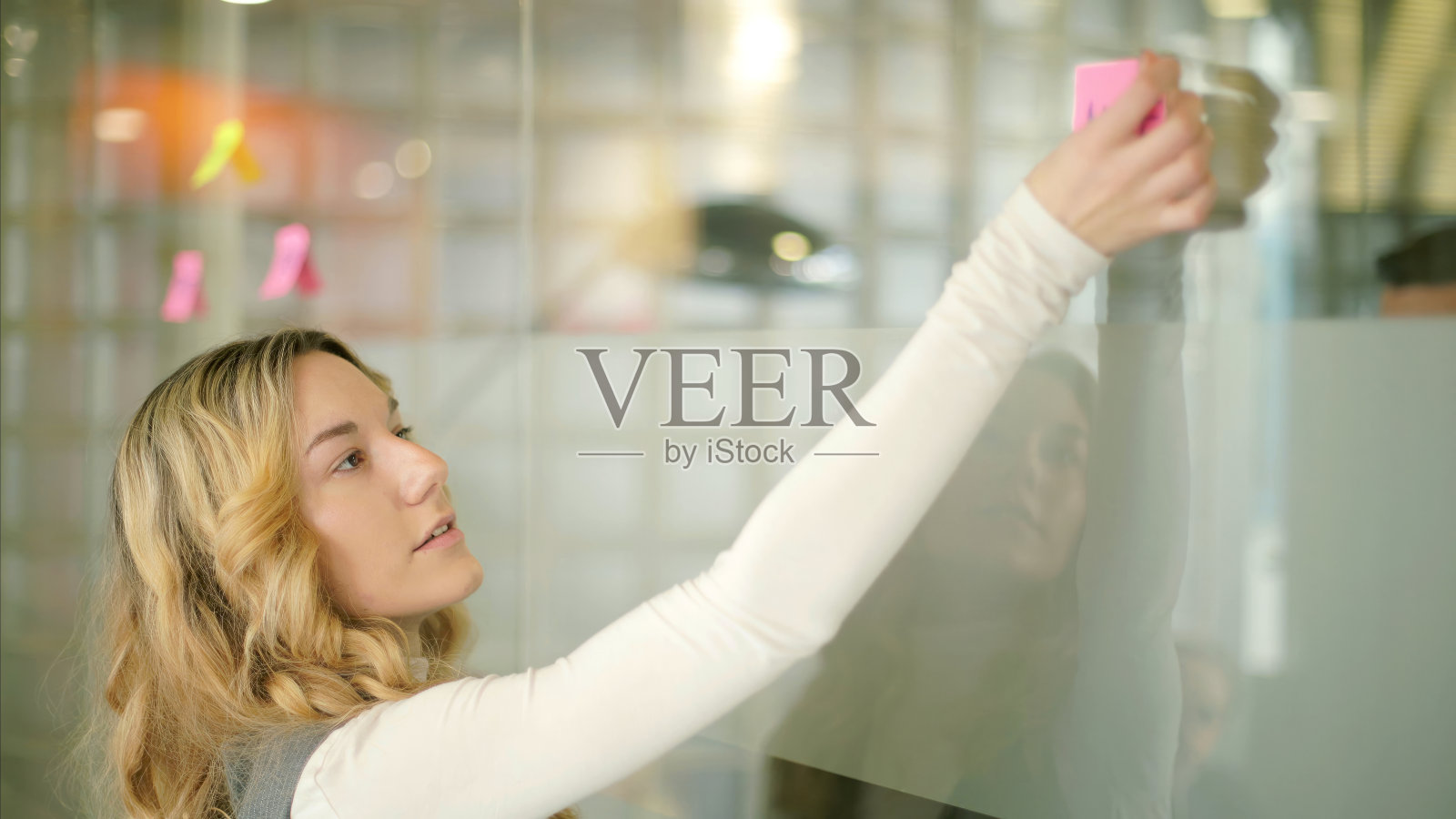 一个女人在明亮的办公室里把便利贴贴在玻璃上照片摄影图片