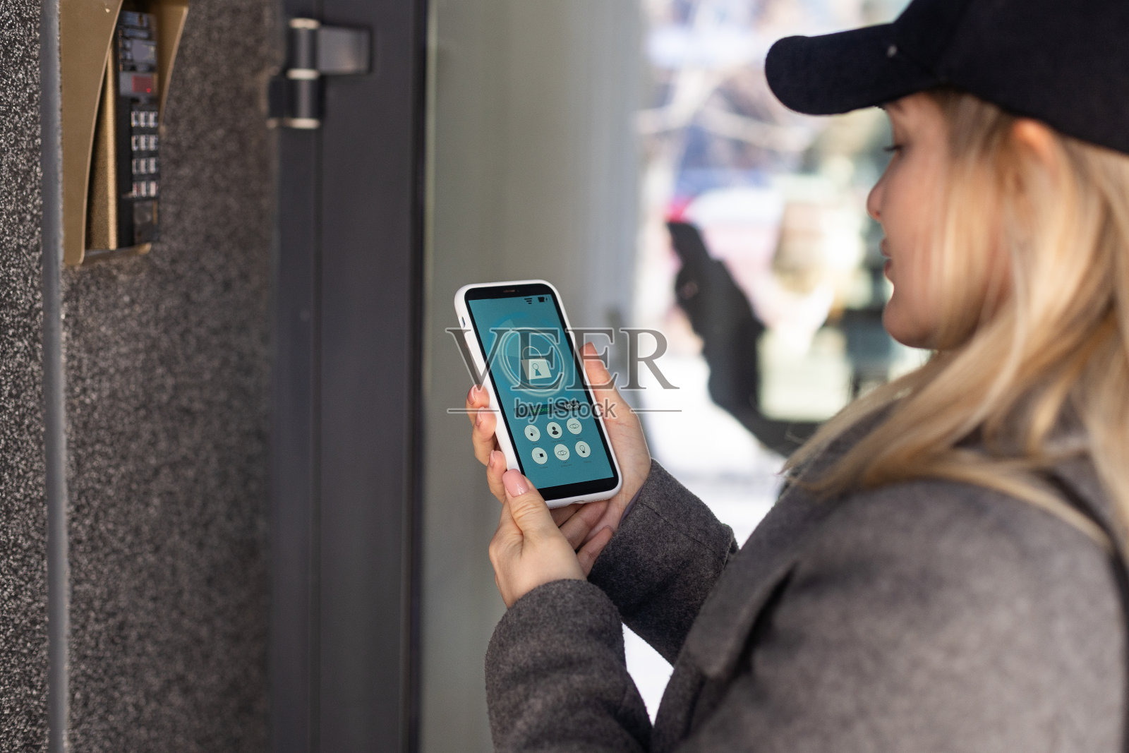 女性手持黑色智能手机，屏幕上有智能家居应用。背景上模糊的房子。为了进入你的房子的所有控制和家庭安全的关怀照片摄影图片