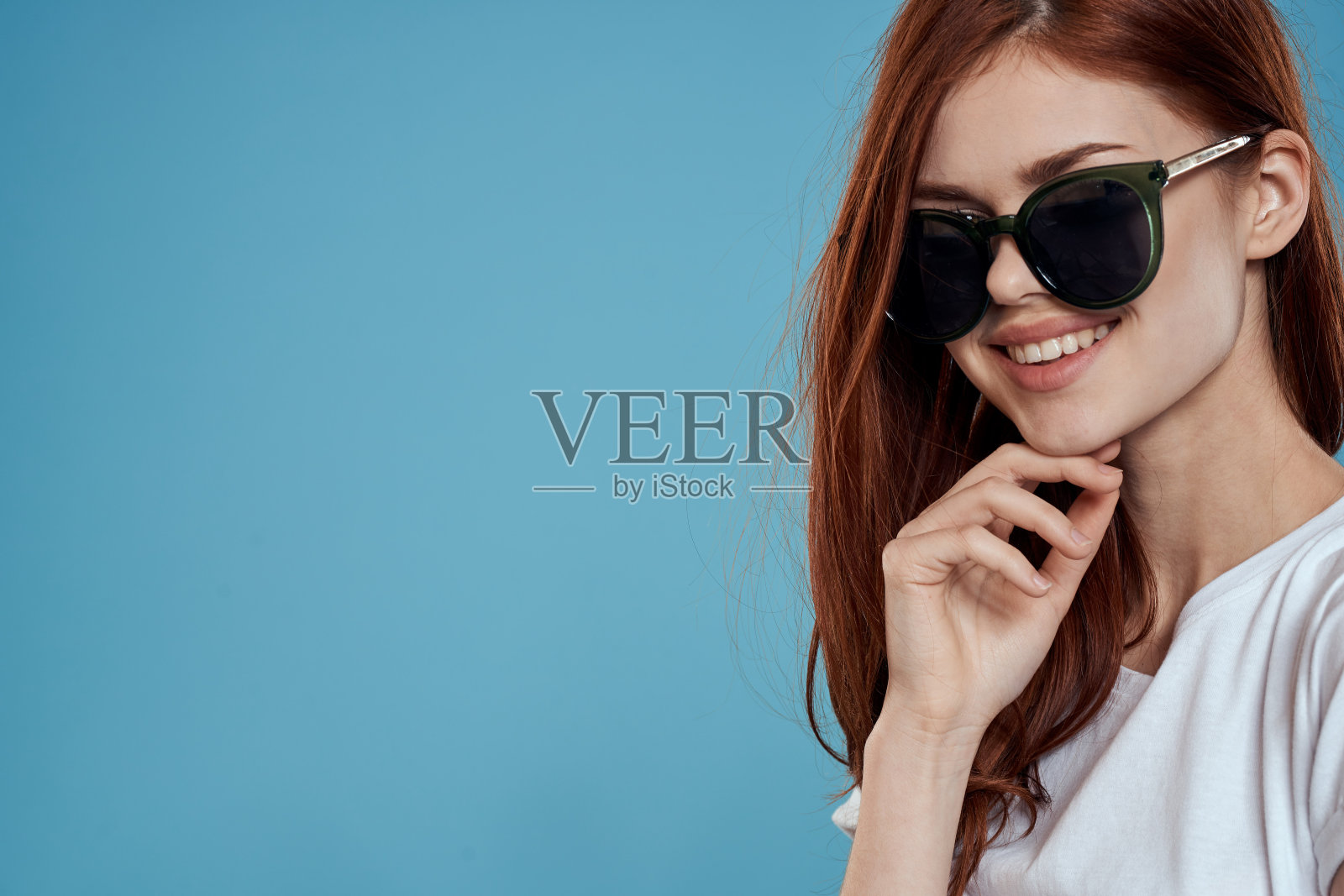 漂亮的女人戴着太阳镜，长发迷人，白色t恤，蓝色背景照片摄影图片