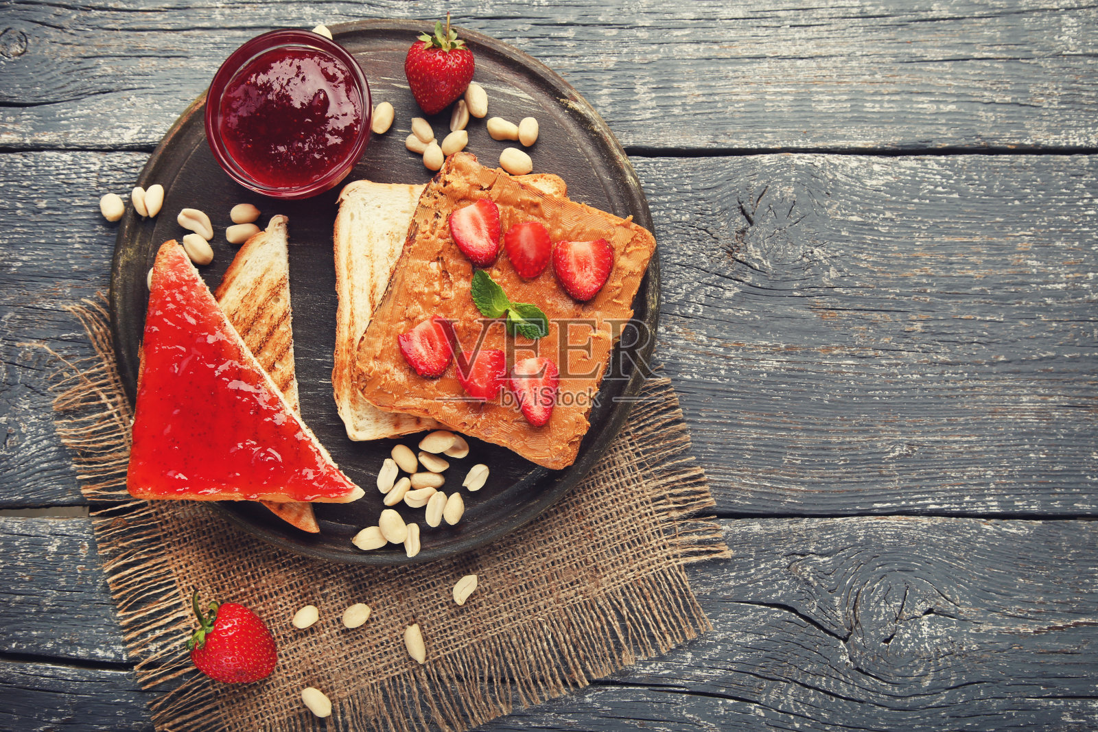 面包配花生酱、果酱、水果和坚果放在灰色的木桌上照片摄影图片