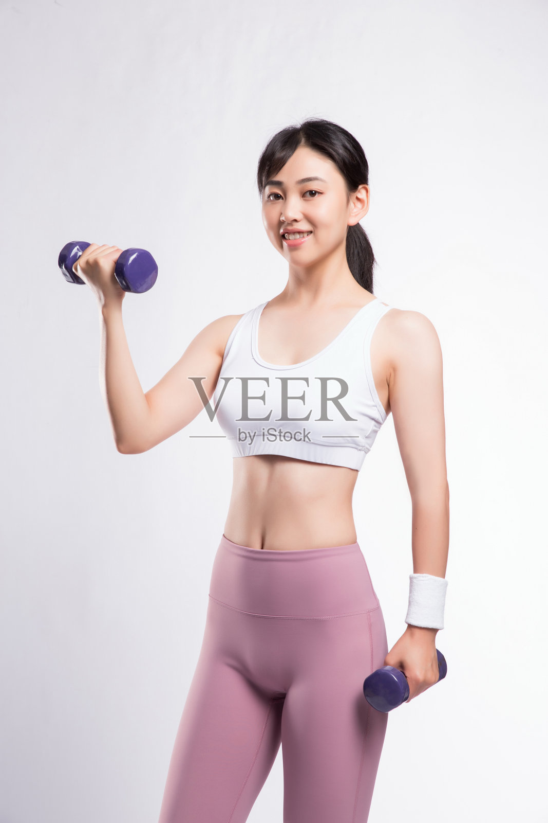 灰色背景前，穿着健身服的亚洲女性用哑铃训练照片摄影图片