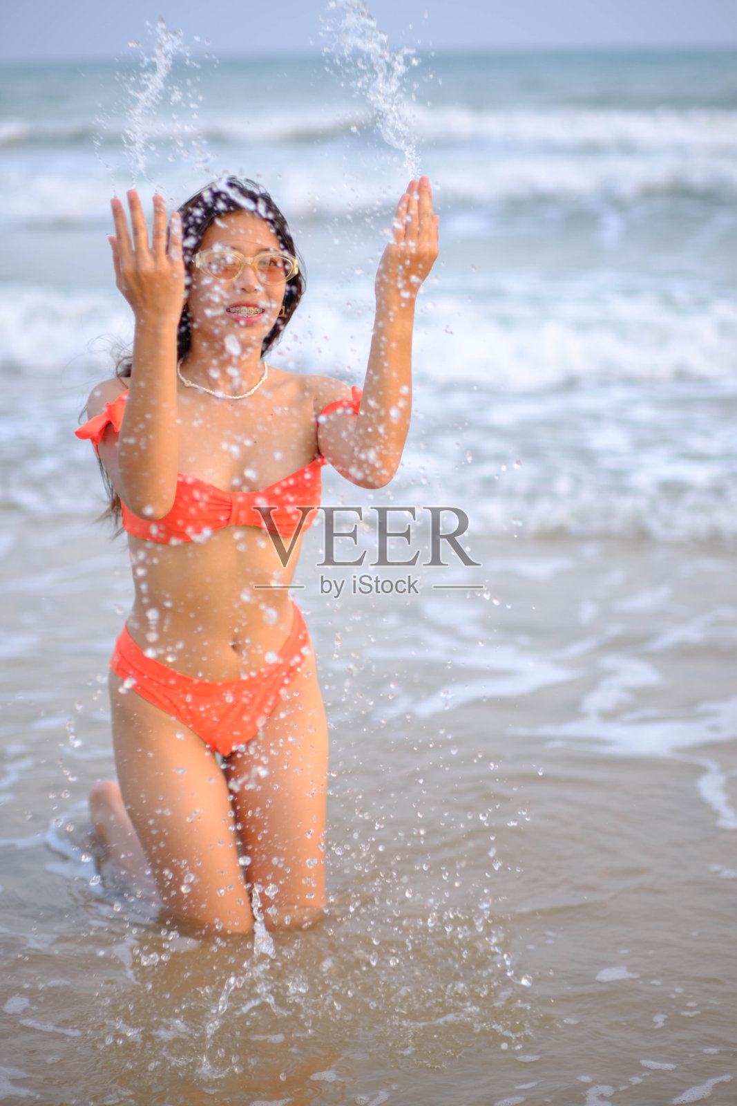 美丽的亚洲女人穿着橙色比基尼坐在水里在海滩上的早晨。照片摄影图片