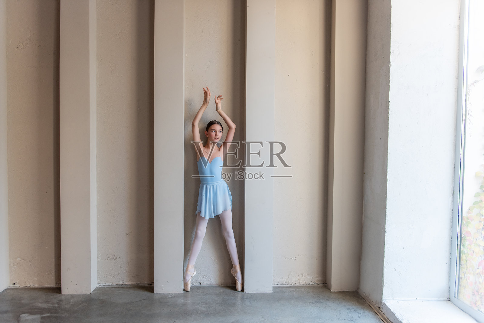 优雅的年轻芭蕾舞女演员身穿蓝色服装，踮着脚尖，轻轻地举起双臂，在阳光下弓着身子照片摄影图片